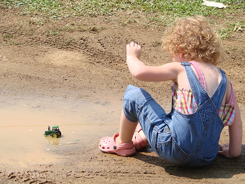 girl with feet and toy truck in mud puddle